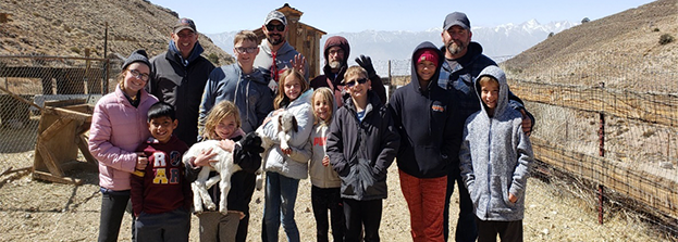 Group of adults and kids, including one holding a baby goat, on a weekend event in the desert